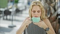 Young blonde woman drinking cup of coffee sitting on table at coffee shop terrace Royalty Free Stock Photo