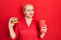 Young blonde woman eating a tasty classic burger with fries and soda smiling looking to the side and staring away thinking Royalty Free Stock Photo