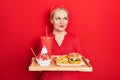 Young blonde woman eating a tasty classic burger with fries and soda smiling looking to the side and staring away thinking Royalty Free Stock Photo