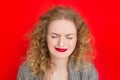 Young blonde woman with green eyes crying over red background. Close up portrait of student curly girl. Expressive facial emotions Royalty Free Stock Photo