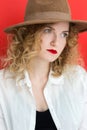 Young blonde woman with green eyes wearing in hat and white shirt over red background. Close up portrait of student curly girl. Royalty Free Stock Photo