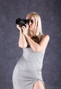 Young blonde woman in grey dress holding camera. Photographer making pictures. Royalty Free Stock Photo