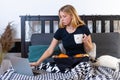 Young blonde woman having breakfast in bed, drinking coffee and and read the news on laptop Royalty Free Stock Photo