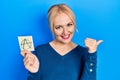 Young blonde woman holding anarchism drawing reminder pointing thumb up to the side smiling happy with open mouth