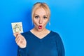 Young blonde woman holding anarchism drawing reminder scared and amazed with open mouth for surprise, disbelief face