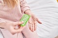 Young blonde woman holding birth control pills sitting on bed at bedroom Royalty Free Stock Photo