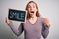 Young blonde woman holding blackboard with smile message over isolated white background screaming proud and celebrating victory Royalty Free Stock Photo