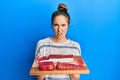 Young blonde woman holding board with raw meat in shock face, looking skeptical and sarcastic, surprised with open mouth Royalty Free Stock Photo