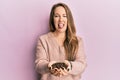 Young blonde woman holding coffee beans with hands sticking tongue out happy with funny expression