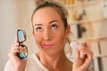 Young blonde woman holding contact lens case on hand and holding in her other hand a blue glasses on blurred background Royalty Free Stock Photo