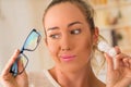 Young blonde woman holding contact lens case on hand and holding in her other hand a blue glasses on blurred background Royalty Free Stock Photo