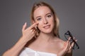 Young blonde woman holding contact lens on finger in front of her face and holding in her other hand a black glasses on Royalty Free Stock Photo