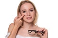 Young blonde woman holding contact lens on finger in front of her face and holding in her other hand a black glasses on Royalty Free Stock Photo