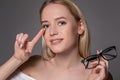 Young blonde woman holding contact lens on finger in front of her face and holding in her other hand a black glasses on Royalty Free Stock Photo