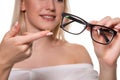 Young blonde woman holding contact lens on finger in front of her face and holding in her other hand a black glasses on Royalty Free Stock Photo