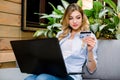 Young blonde woman holding credit card and using laptop computer. Online shopping concept, travelling, booking tickets Royalty Free Stock Photo
