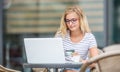 Young blonde woman holding credit card and using laptop computeron the terrace of the caf