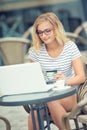 Young blonde woman holding credit card and using laptop computeron the terrace of the caf