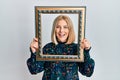 Young blonde woman holding empty frame smiling and laughing hard out loud because funny crazy joke Royalty Free Stock Photo