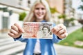 Young blonde woman holding english banknotes pounds, showing money smiling happy and confident outdoors