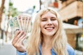 Young blonde woman holding english banknotes pounds, showing money smiling happy and confident outdoors