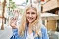 Young blonde woman holding english banknotes pounds, showing money smiling happy and confident outdoors