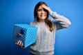 Young blonde woman holding a gift box as birthday present over isolated background stressed with hand on head, shocked with shame Royalty Free Stock Photo