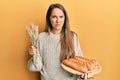 Young blonde woman holding homemade bread and spike wheat skeptic and nervous, frowning upset because of problem