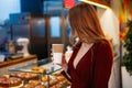 Young blonde woman holding a paper cup of hot coffee of takeaway in her hands indoors in cafe and looking in camera. copyspace. Royalty Free Stock Photo