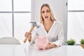 Young blonde woman holding piggy bank and hammer clueless and confused expression Royalty Free Stock Photo