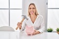 Young blonde woman holding piggy bank and hammer sticking tongue out happy with funny expression Royalty Free Stock Photo