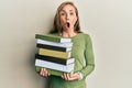 Young blonde woman holding a pile of books afraid and shocked with surprise and amazed expression, fear and excited face Royalty Free Stock Photo