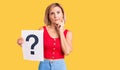 Young blonde woman holding question mark serious face thinking about question with hand on chin, thoughtful about confusing idea Royalty Free Stock Photo