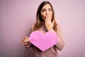 Young blonde woman holding romantic big paper heart shape over pink isolated background cover mouth with hand shocked with shame Royalty Free Stock Photo