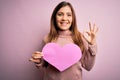 Young blonde woman holding romantic big paper heart shape over pink isolated background doing ok sign with fingers, excellent Royalty Free Stock Photo