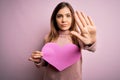 Young blonde woman holding romantic big paper heart shape over pink isolated background with open hand doing stop sign with Royalty Free Stock Photo