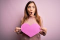 Young blonde woman holding romantic big paper heart shape over pink isolated background scared in shock with a surprise face, Royalty Free Stock Photo