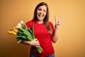 Young blonde woman holding romantic bouquet of tulips flowers over yellow background smiling with happy face winking at the camera Royalty Free Stock Photo