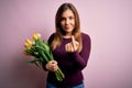 Young blonde woman holding romantic bouquet of yellow tulips flowers over pink background Beckoning come here gesture with hand Royalty Free Stock Photo