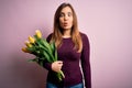 Young blonde woman holding romantic bouquet of yellow tulips flowers over pink background making fish face with lips, crazy and Royalty Free Stock Photo