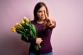 Young blonde woman holding romantic bouquet of yellow tulips flowers over pink background Pointing with finger up and angry Royalty Free Stock Photo