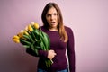 Young blonde woman holding romantic bouquet of yellow tulips flowers over pink background In shock face, looking skeptical and Royalty Free Stock Photo