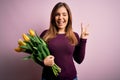 Young blonde woman holding romantic bouquet of yellow tulips flowers over pink background smiling with happy face winking at the Royalty Free Stock Photo