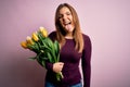 Young blonde woman holding romantic bouquet of yellow tulips flowers over pink background sticking tongue out happy with funny Royalty Free Stock Photo