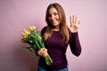 Young blonde woman holding romantic bouquet of yellow tulips flowers over pink background Waiving saying hello happy and smiling, Royalty Free Stock Photo