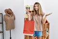 Young blonde woman holding shopping bags trying sunglasses on celebrating achievement with happy smile and winner expression with