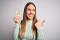 Young blonde woman holding sticky paper note with sad face emoticon over isolated background pointing and showing with thumb up to