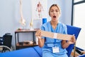 Young blonde woman holding therapy corset afraid and shocked with surprise and amazed expression, fear and excited face Royalty Free Stock Photo