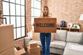 Young blonde woman holding welcome doormat at new home afraid and shocked with surprise and amazed expression, fear and excited Royalty Free Stock Photo