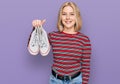 Young blonde woman holding white casual shoes looking positive and happy standing and smiling with a confident smile showing teeth Royalty Free Stock Photo